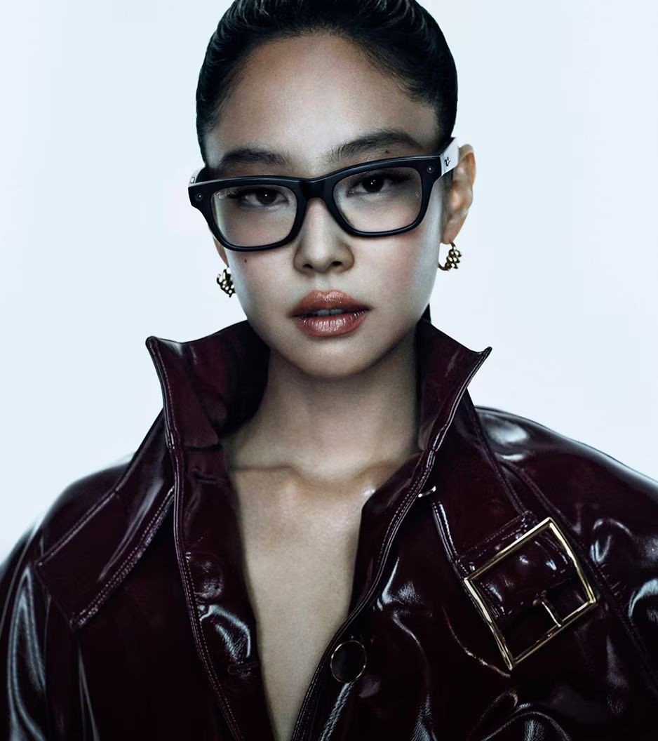 Retrato de una persona con gafas negras y una chaqueta de cuero color burdeos sobre un fondo claro liso.