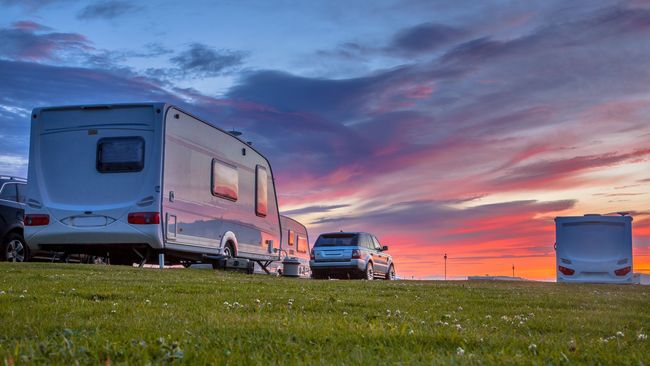 Des camping-cars et une camionnette garés sur l'herbe sous un ciel de coucher de soleil aux couleurs chatoyantes.