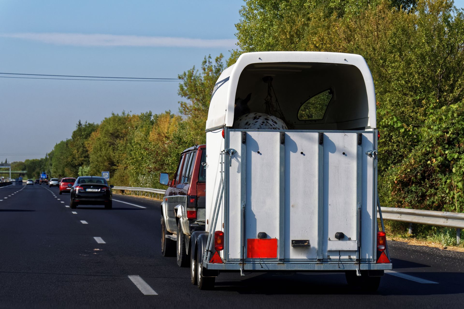 Une voiture rouge circulant sur une autoroute, avec une remorque blanche à plateau au premier plan.