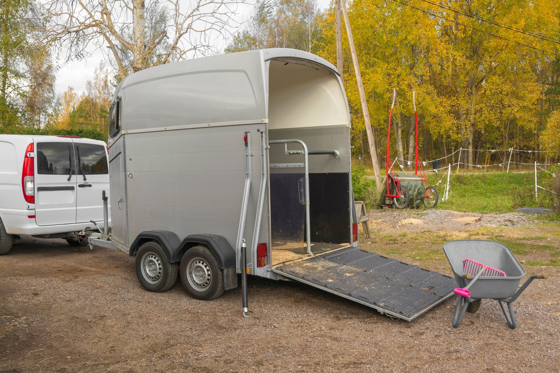 Remorque blanche pour chevaux avec rampe à côté d'une camionnette blanche dans un espace boisé extérieur.