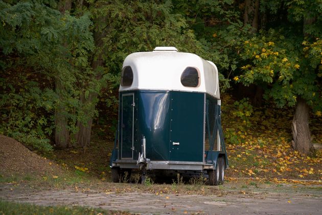 Toilettes portables bleues et blanches sur un chemin de gravier dans une zone boisée
