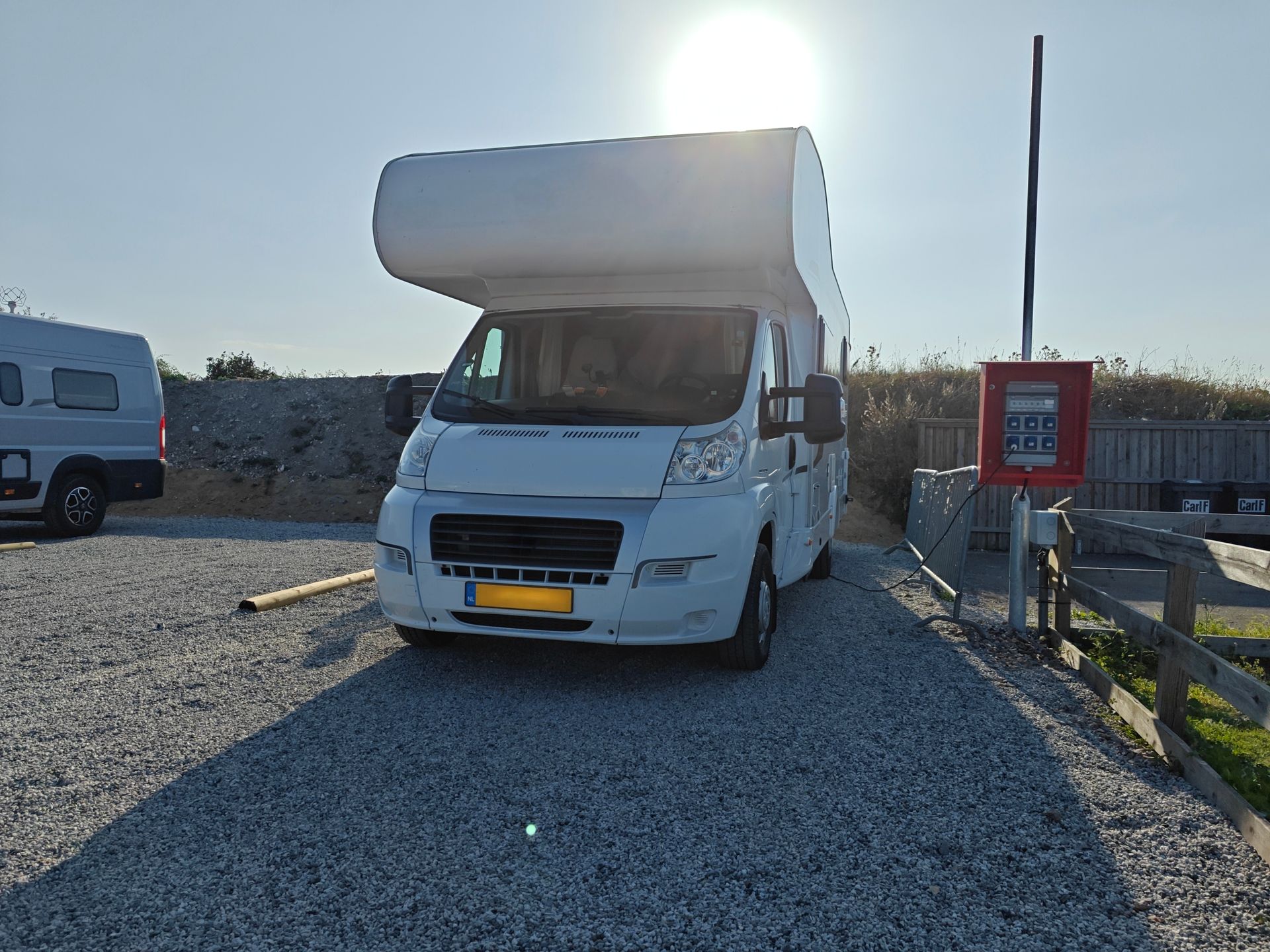 Un camping-car blanc garé sur du gravier, près d'une clôture, en plein soleil.
