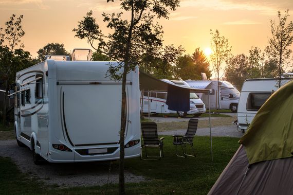 Des camping-cars dans un camping au coucher du soleil, avec des chaises et des arbres.