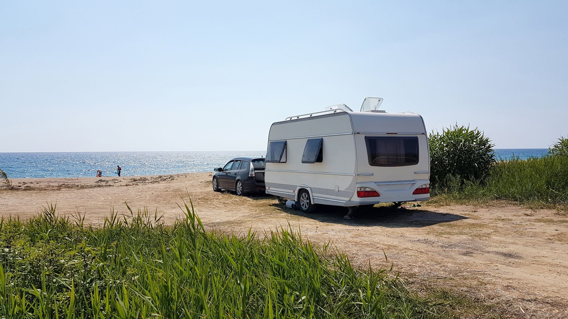 Un camping-car blanc est garé sur une plage de gravier, avec la mer en arrière-plan.