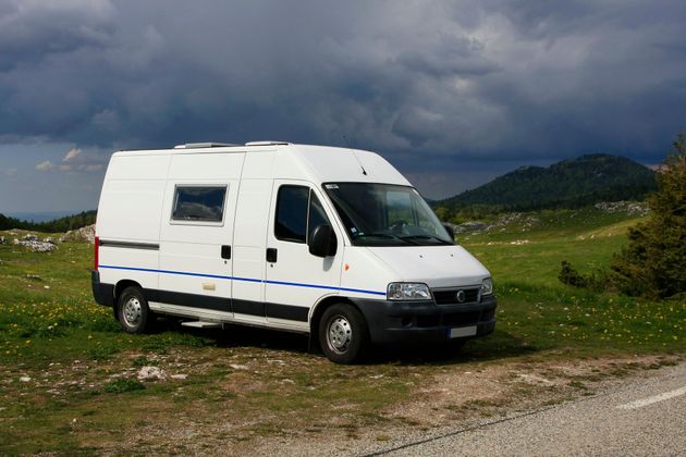 Une camionnette blanche garée sur un chemin de terre herbeux sous un ciel orageux, avec des collines en arrière-plan.