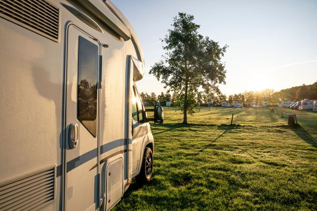 Un camping-car garé dans un champ herbeux au coucher du soleil, avec un arbre et un paysage ouvert à l'horizon.