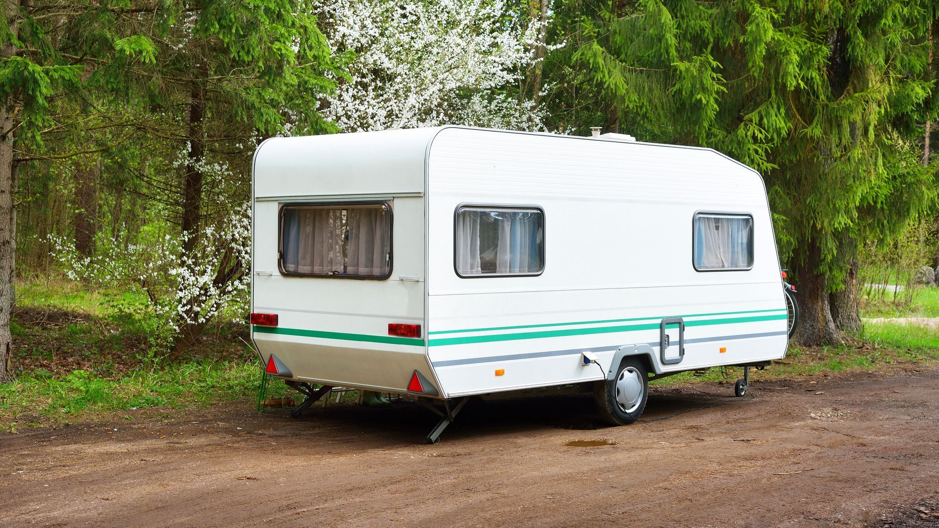 Une caravane blanche est garée sur un chemin de terre dans une zone boisée.