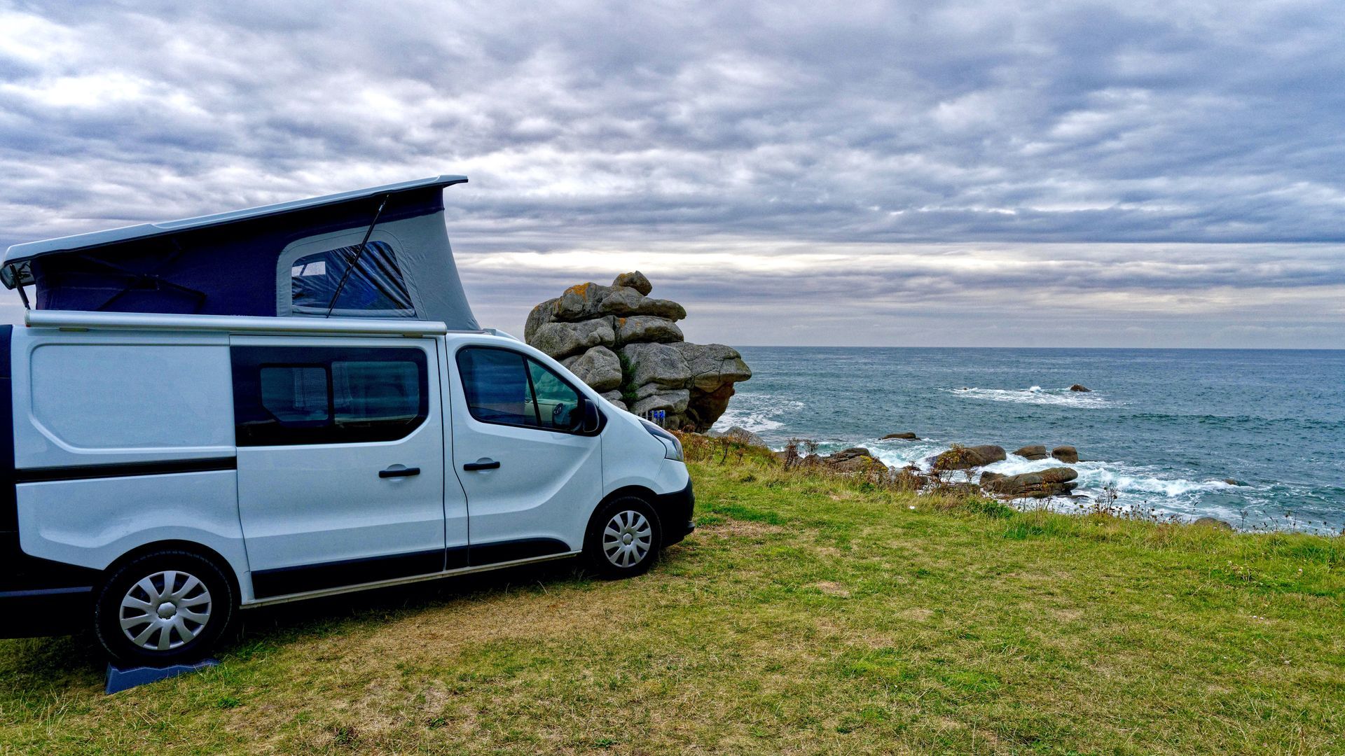 Un camping-car blanc garé sur une côte herbeuse au bord de l'océan, sous un ciel nuageux