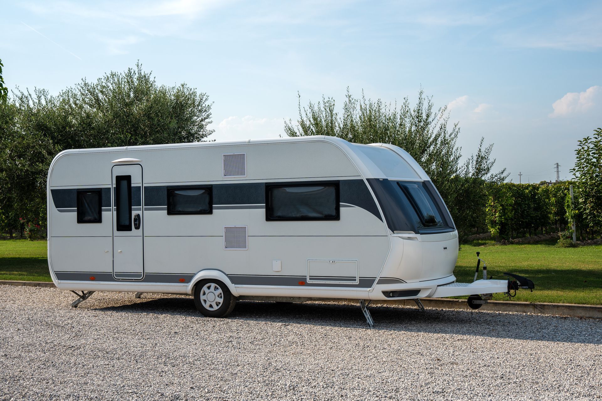 Caravane blanche garée sur du gravier, avec de l'herbe et des arbres en arrière-plan.