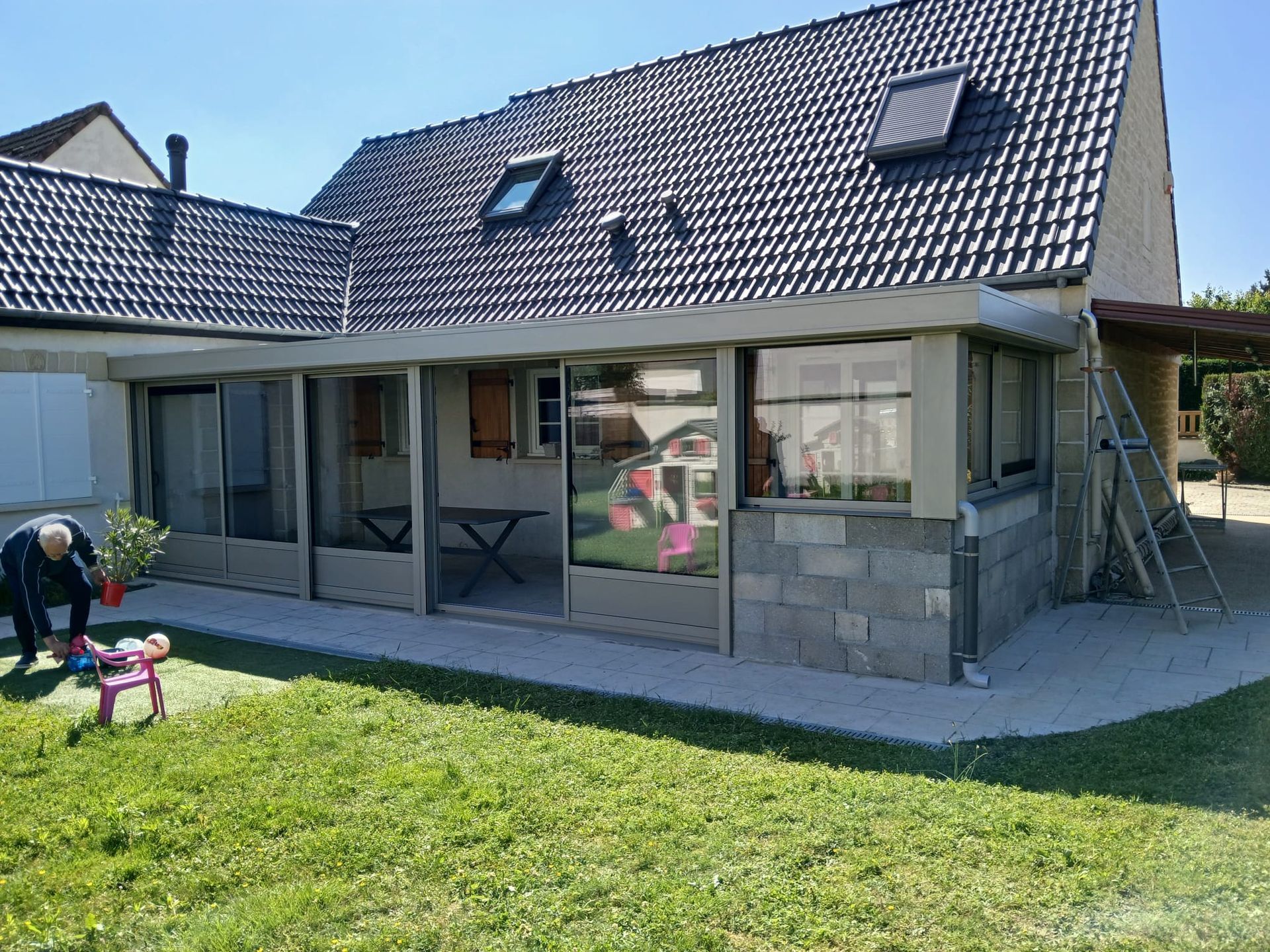 Véranda en aluminium avec les parois vitrées et un muret maçonné.