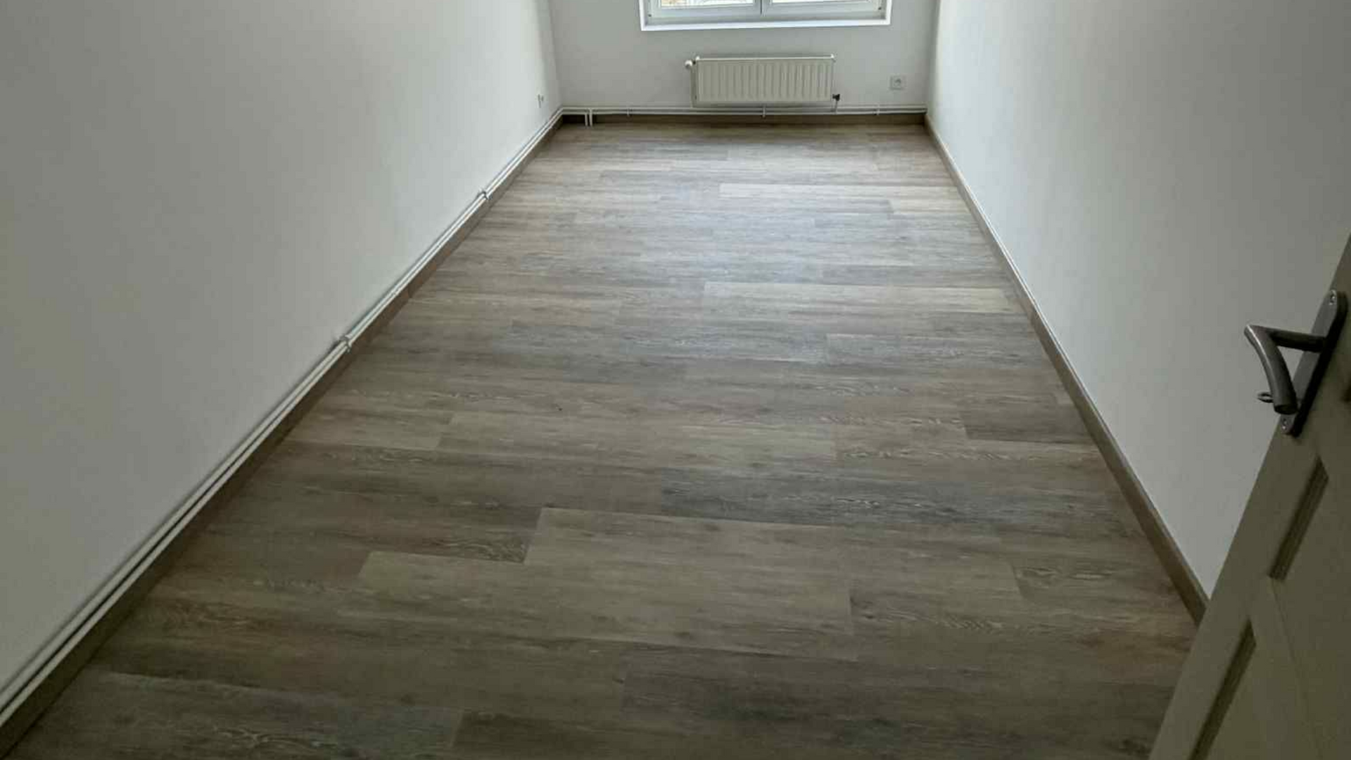 Pièce vide avec sol en parquet et murs blancs.