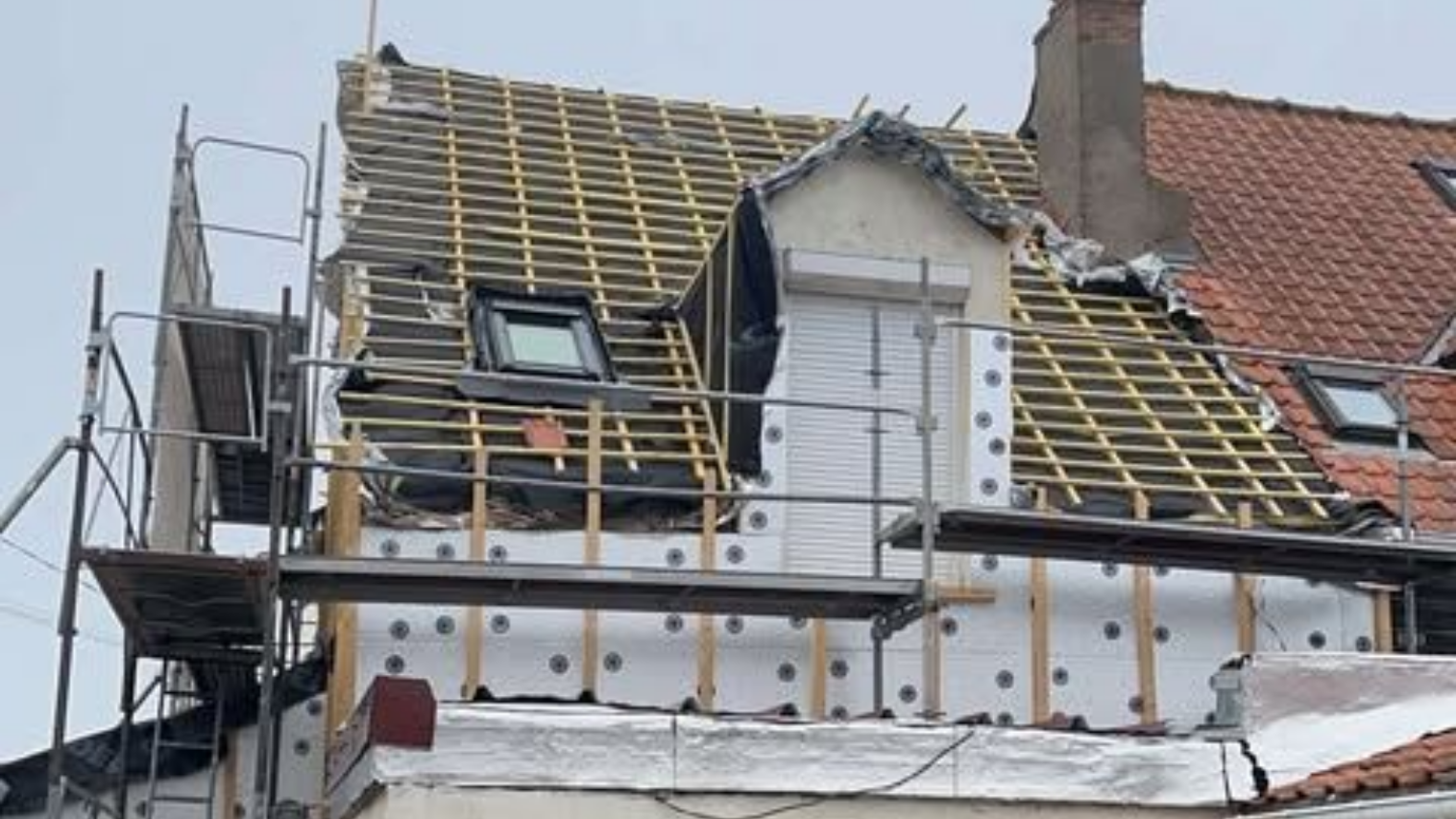 Toiture d'un bâtiment en construction. Échafaudages, poutres en bois apparentes et isolation visibles.