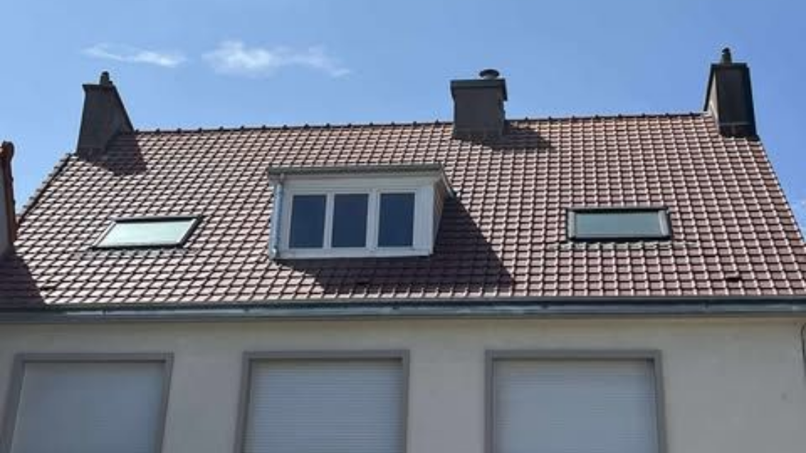 Une maison avec une façade beige et toit de tuiles rouges avec et puits de lumière.