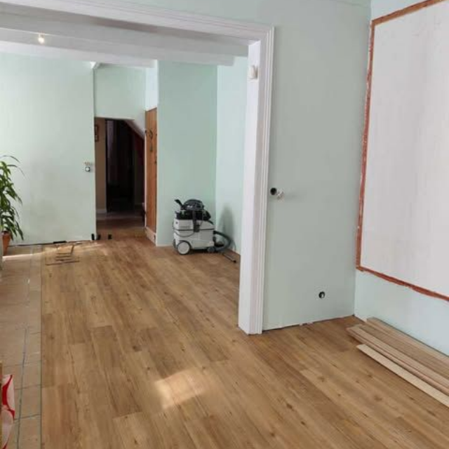 Une personne installe un revêtement de sol imitation bois à côté d'un mur blanc.