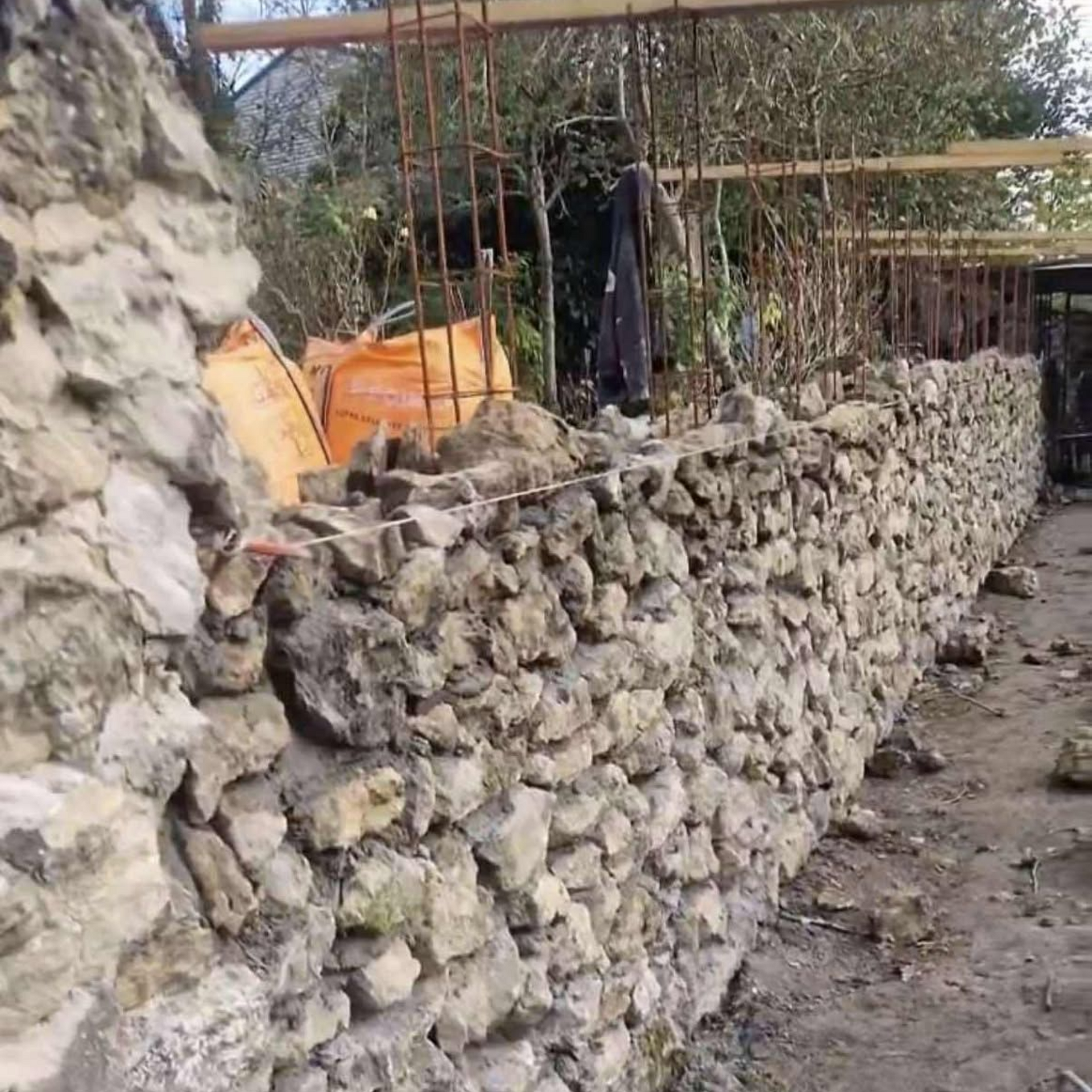 Mur en pierre en construction, avec armatures apparentes et supports en bois.