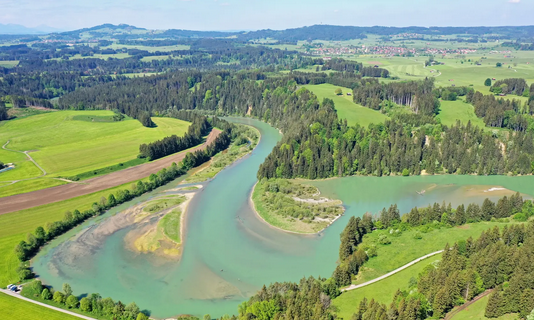 Unter strahlend blauem Himmel schlängelt sich ein Fluss durch üppig grünes Ackerland und Wälder.