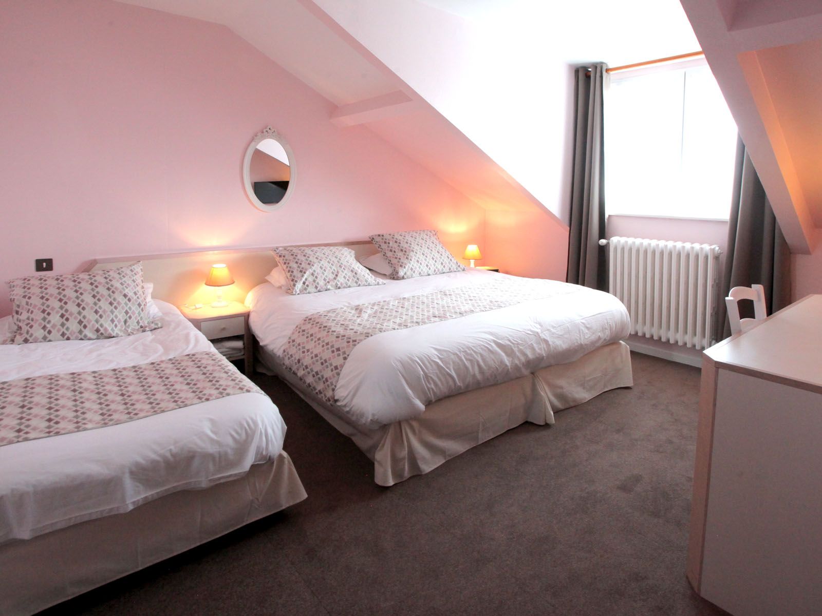 Une chambre d'hotel au mur rose avec deux lits doubles.