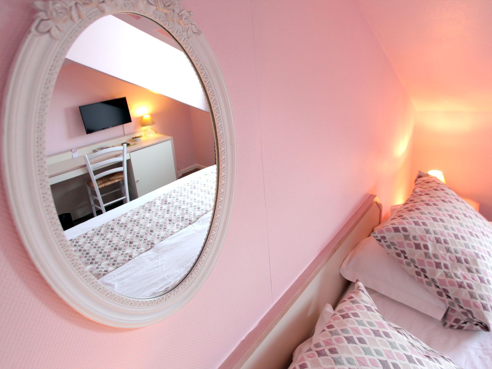 Une chambre d'hotel aux murs rose avec un mirroir ovale.