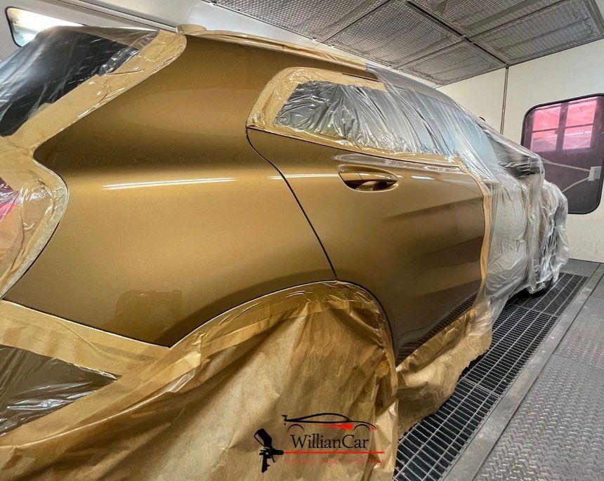 Coche repintado en dorado en cabina de pintura, enmascarado con cinta adhesiva y papel.