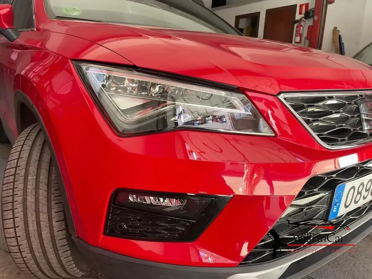Coche rojo, primer plano del frontal. Se ven el faro y la parrilla. Se ven una llanta y la matrícula.