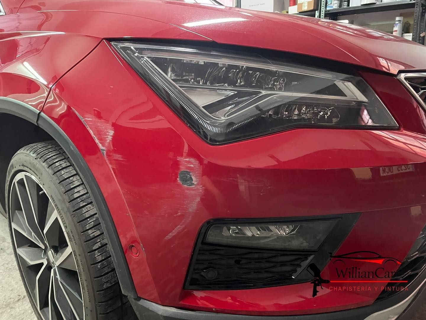 Parte frontal de un automóvil rojo con faro, parachoques dañado y neumático visible.