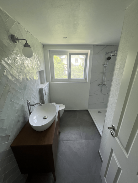 Une salle de bain avec douche, un lavabo, miroir et WC.