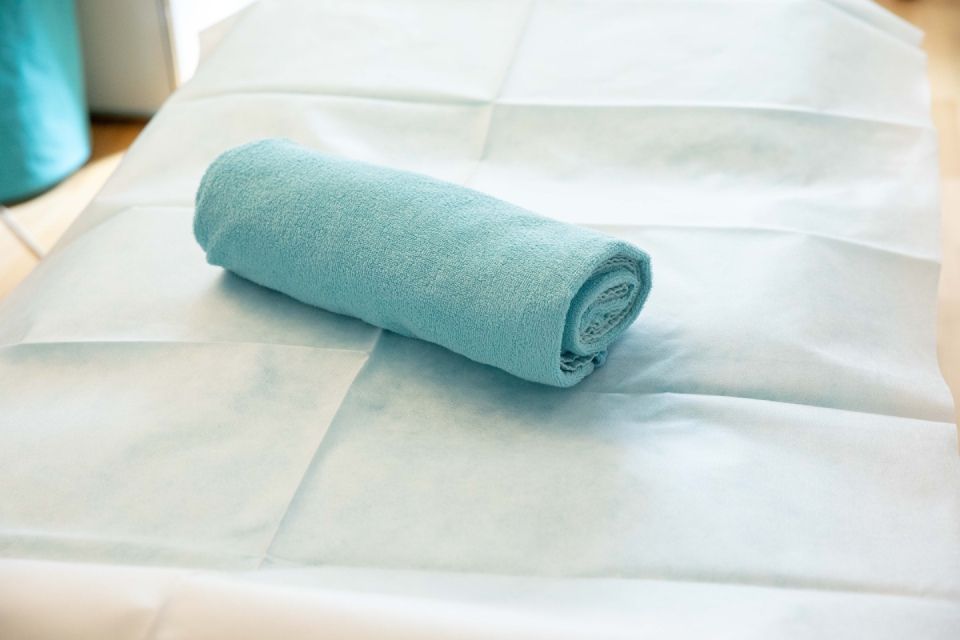Gerolltes blaues Handtuch auf einem mit weißem Papier bedeckten Massagetisch im Innenbereich.