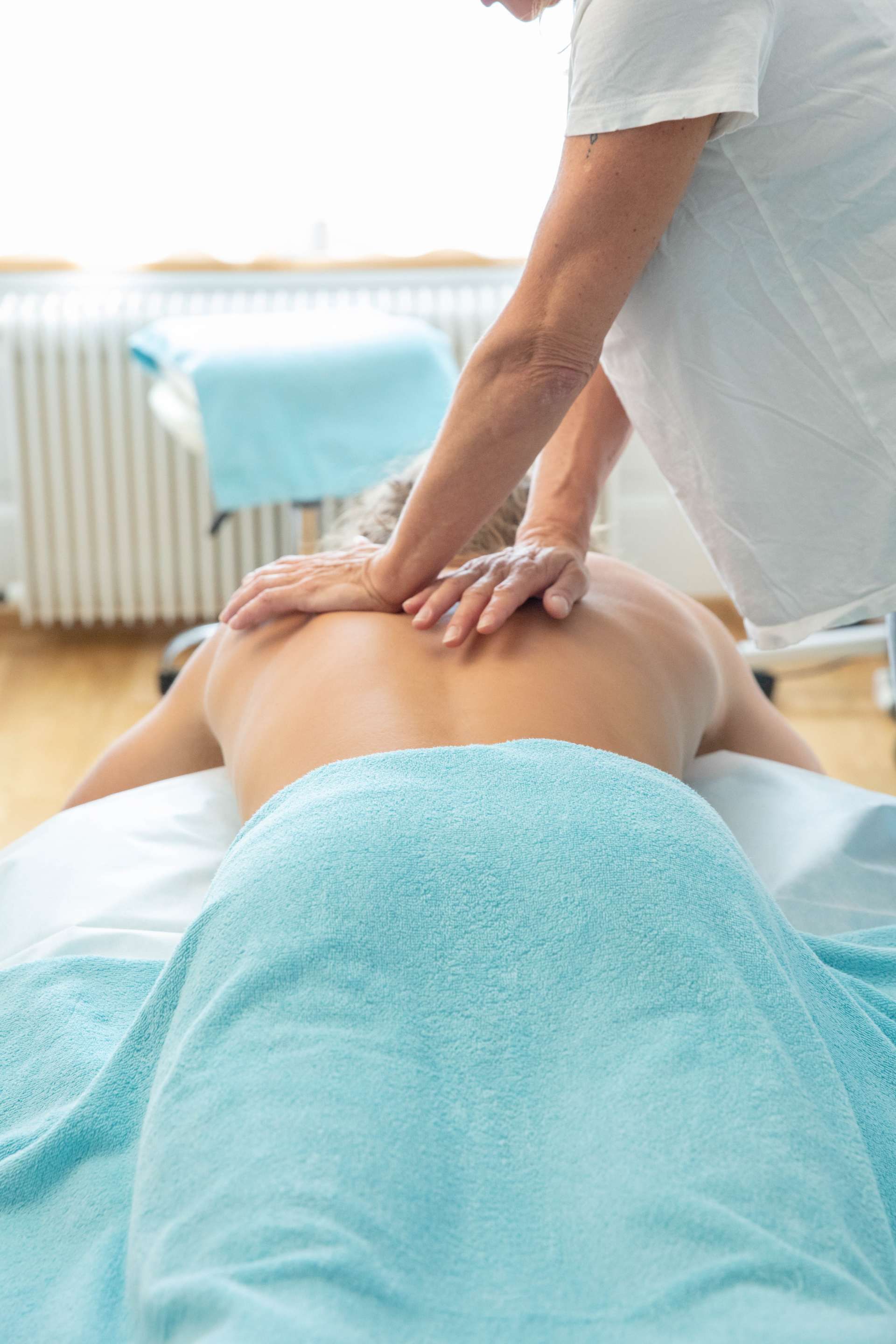 Person, die eine Rückenmassage auf einem Massagetisch erhält, blaues Handtuch, weißes Hemd.