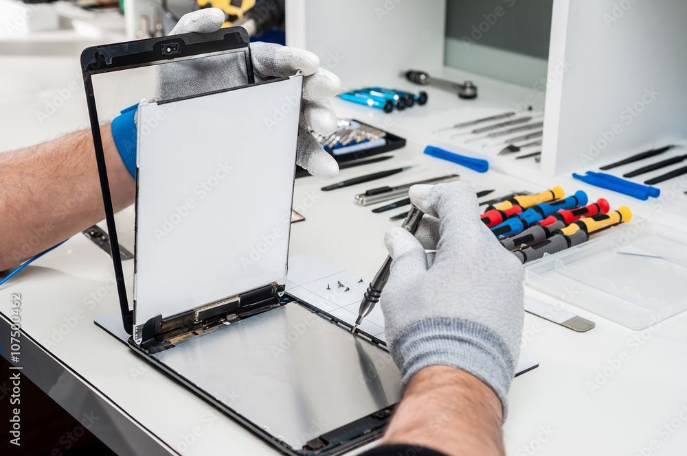 Hände halten einen Tablet-Bildschirm über dem Gerätegehäuse und bereiten ihn auf einer Werkbank zur Reparatur vor.