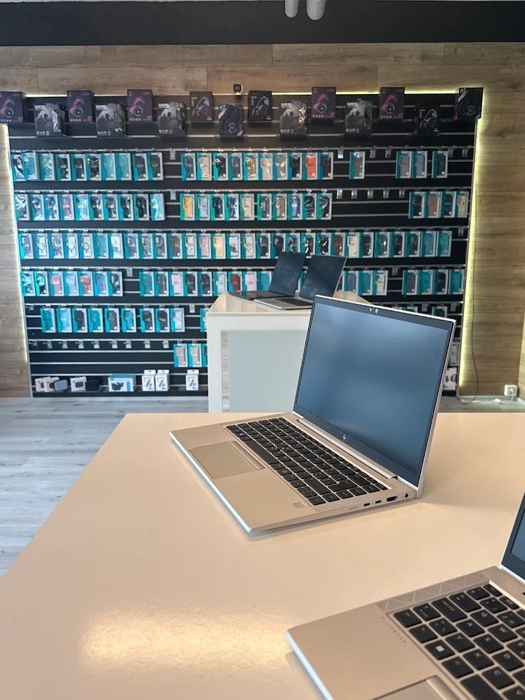 Ein Laptop steht auf einem weissen Tisch in einem Geschäft mit einer Wandauslage voller Handyhüllen und Zubehör.