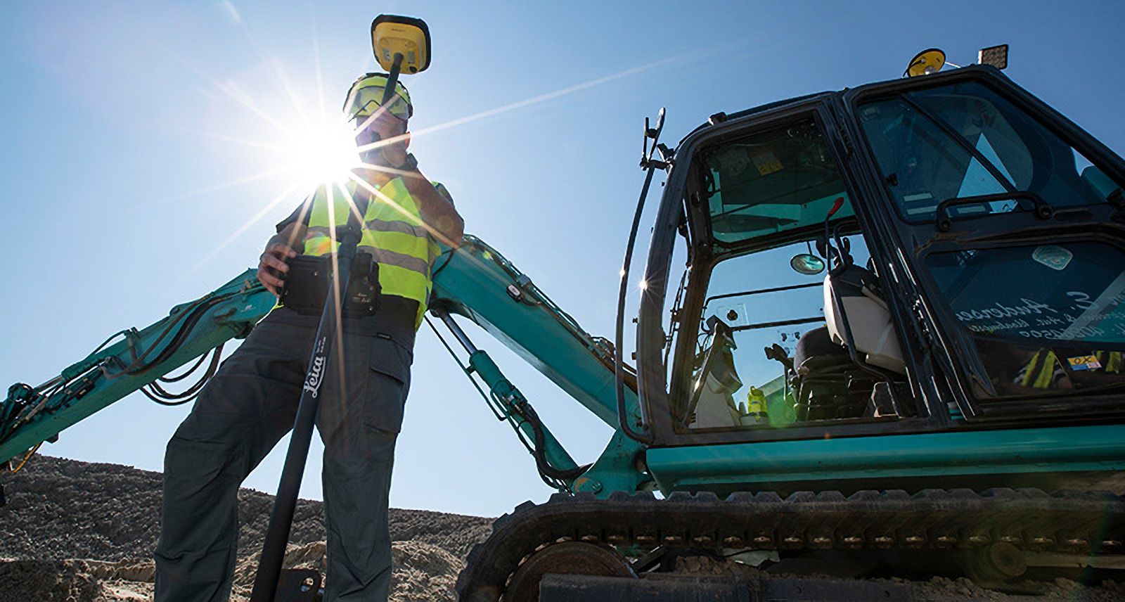 Ein Bauarbeiter steht neben einem blauen Bagger.