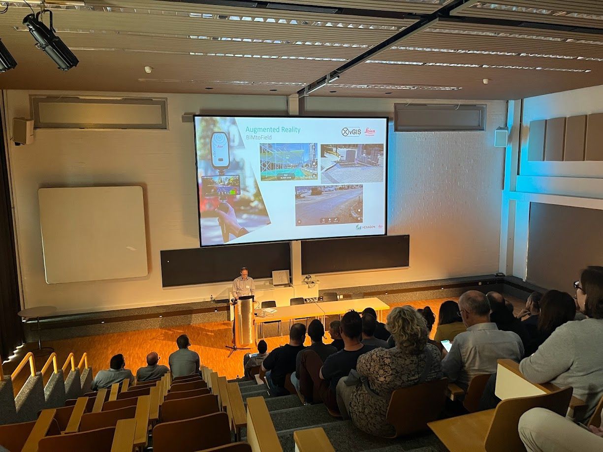 Eine Gruppe von Menschen sitzt in einem Hörsaal und sieht sich eine Präsentation auf einer großen Leinwand an.