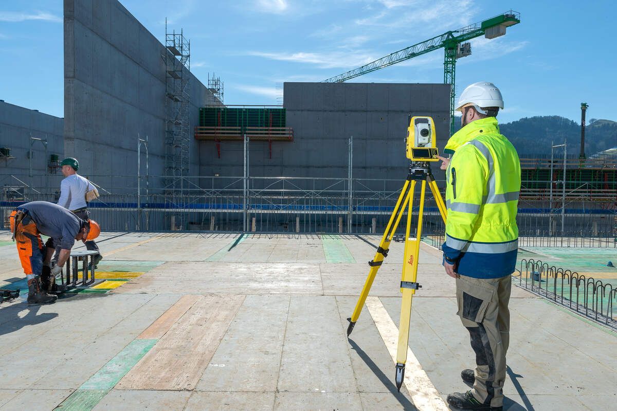 Ein Mann steht mit einem Stativ und einer Kamera auf einer Baustelle.