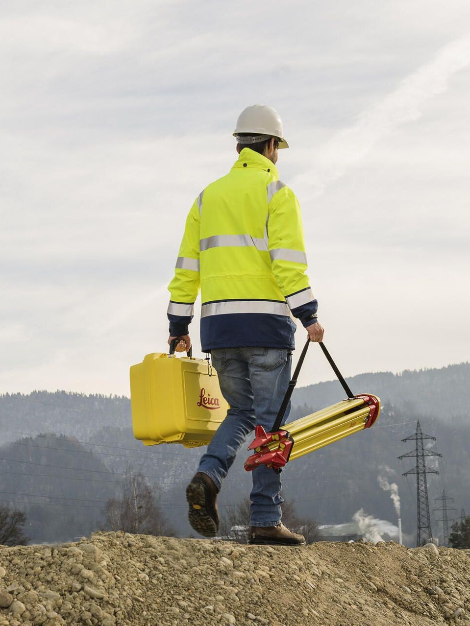 Ein Mann in einer gelben Jacke trägt eine gelbe Kiste und ein Stativ