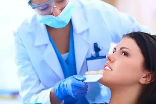 Dentista examinando os dentes de uma mulher com guia de cores. Médica de jaleco branco, máscara e luvas.