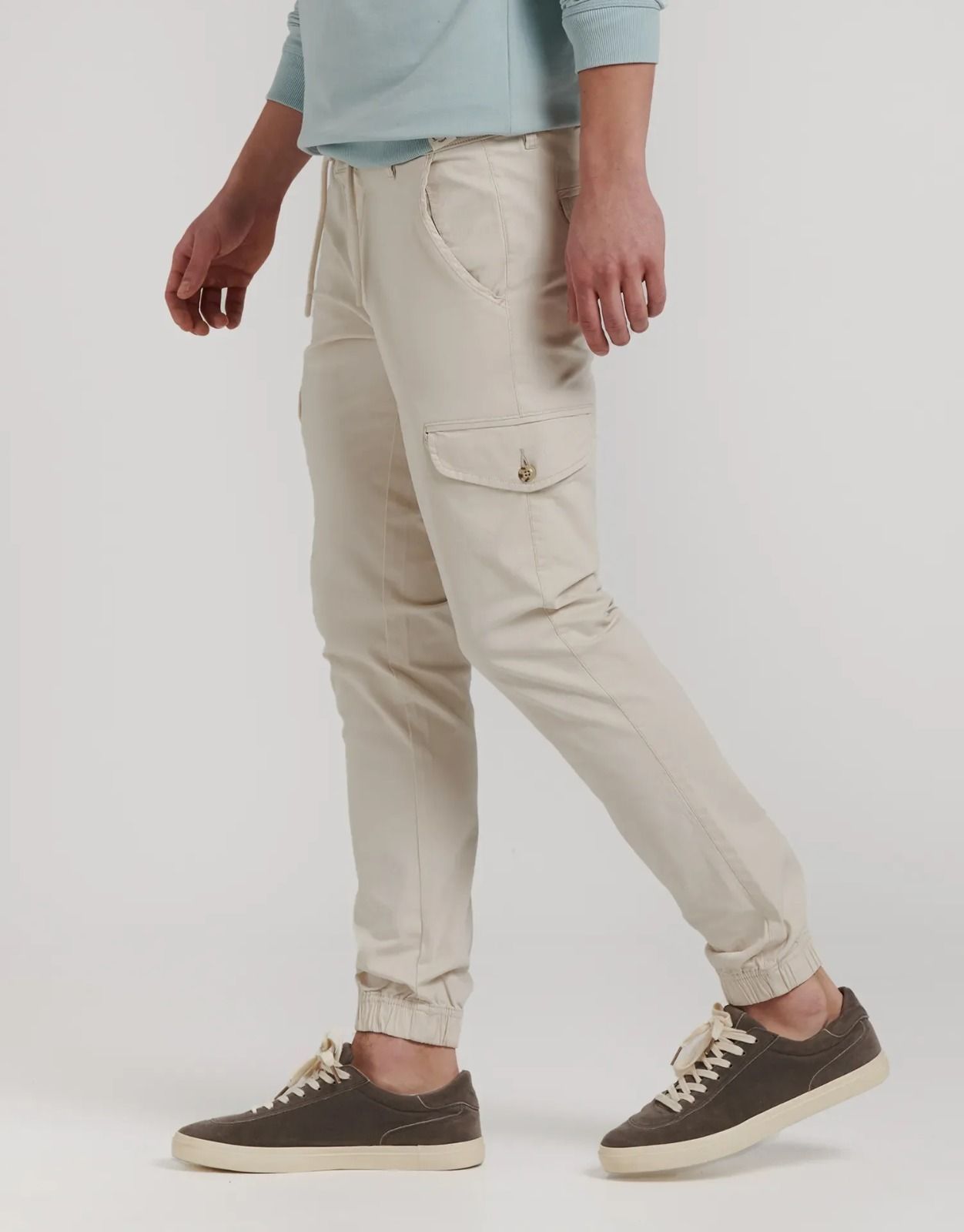 Una persona vestida con pantalones deportivos cargo de color beige y zapatillas oscuras sobre un fondo liso y claro.