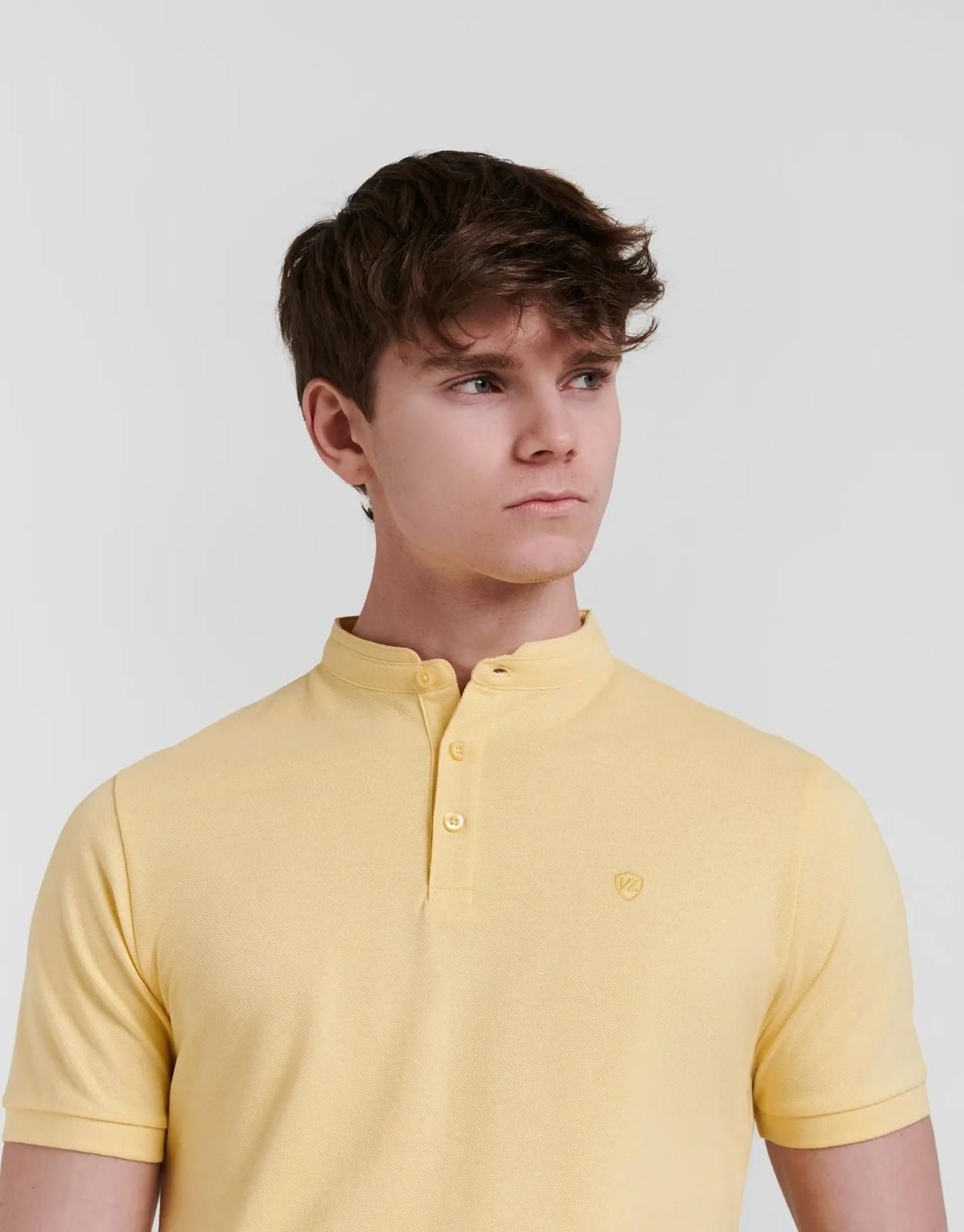 Una persona con una camisa polo amarilla de cuello abotonado posa sobre un fondo claro liso.