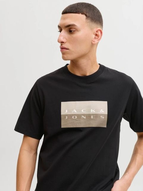 Una persona lleva una camisa marrón abotonada, un suéter beige sobre los hombros y pantalones blancos.