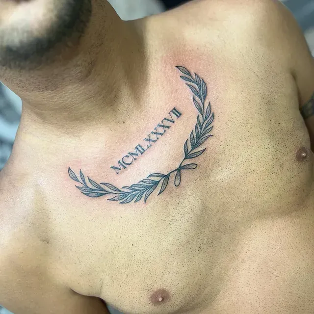 Tatuaje en el pecho: una corona de laurel azul grisácea con números romanos, MCMLXXXVII, en el centro.