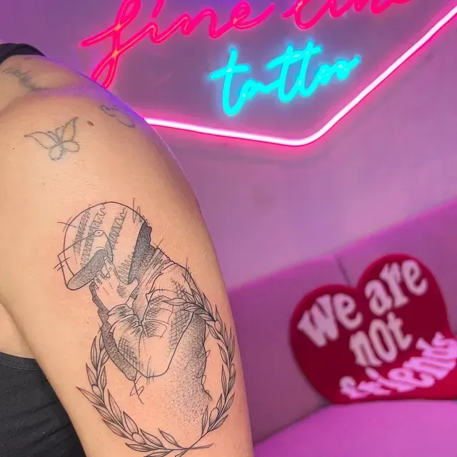 Tatuaje en el brazo de una figura con gorra y corona de laurel, estilo dibujo, cerca de letrero de neón y almohada en forma de corazón.