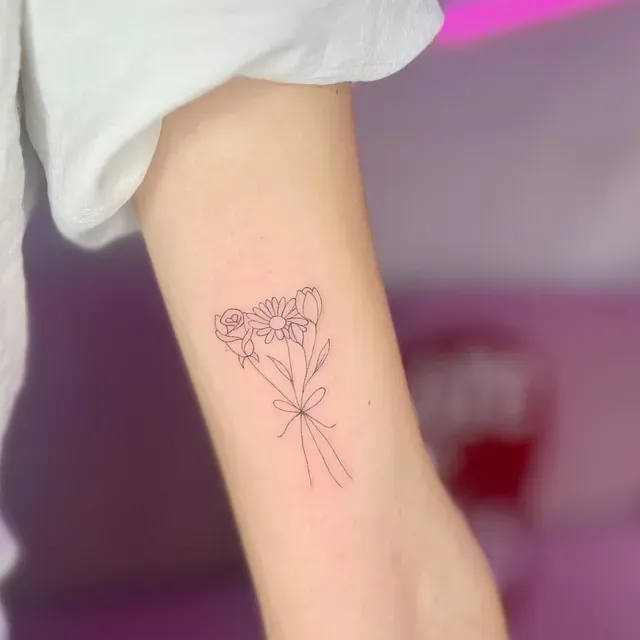 Delicado tatuaje de arte lineal de un ramo de flores atado con un lazo en el antebrazo de una persona.