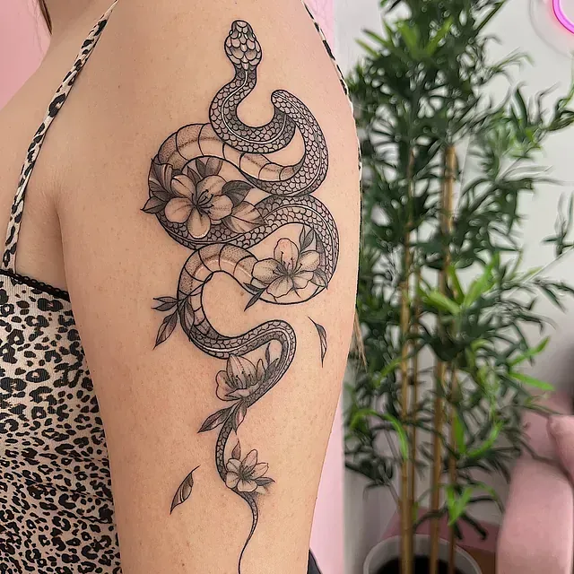 Tatuaje de serpiente negra con flores en la parte superior del brazo de una persona.