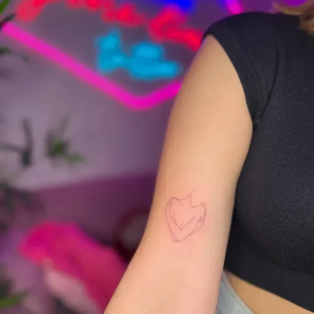 Contorno de una persona abrazándose a sí misma tatuado en el brazo de una mujer.