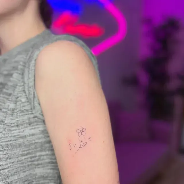 Brazo con un pequeño tatuaje de flor y la palabra