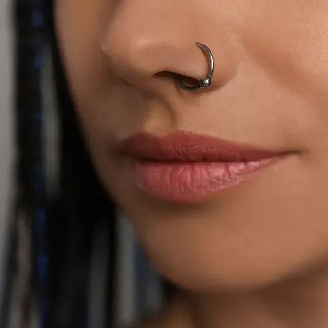 Primer plano de una persona con un piercing en la nariz. Tiene labios rosados y piel suave.