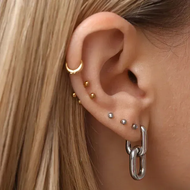 Primer plano de la oreja de una persona con múltiples perforaciones y varios aretes, incluido un diseño de eslabones de cadena.