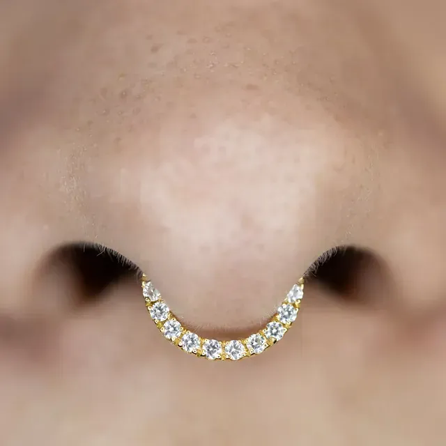 Primer plano de la nariz de una persona con un anillo de tabique de oro incrustado con pequeñas piedras blancas.