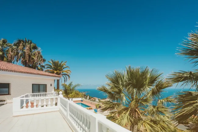 Una casa blanca con balcón con vista al mar y palmeras.