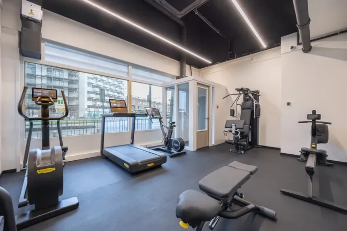 Een sportschool met loopbanden, hometrainers en een bank.