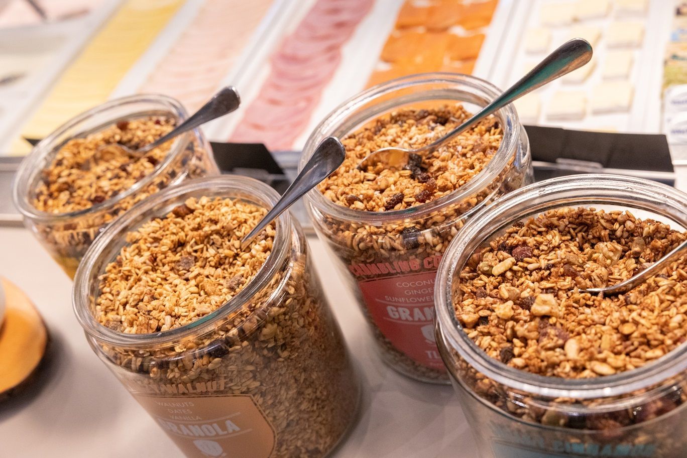 Vier potten granola met lepels erin op tafel.
